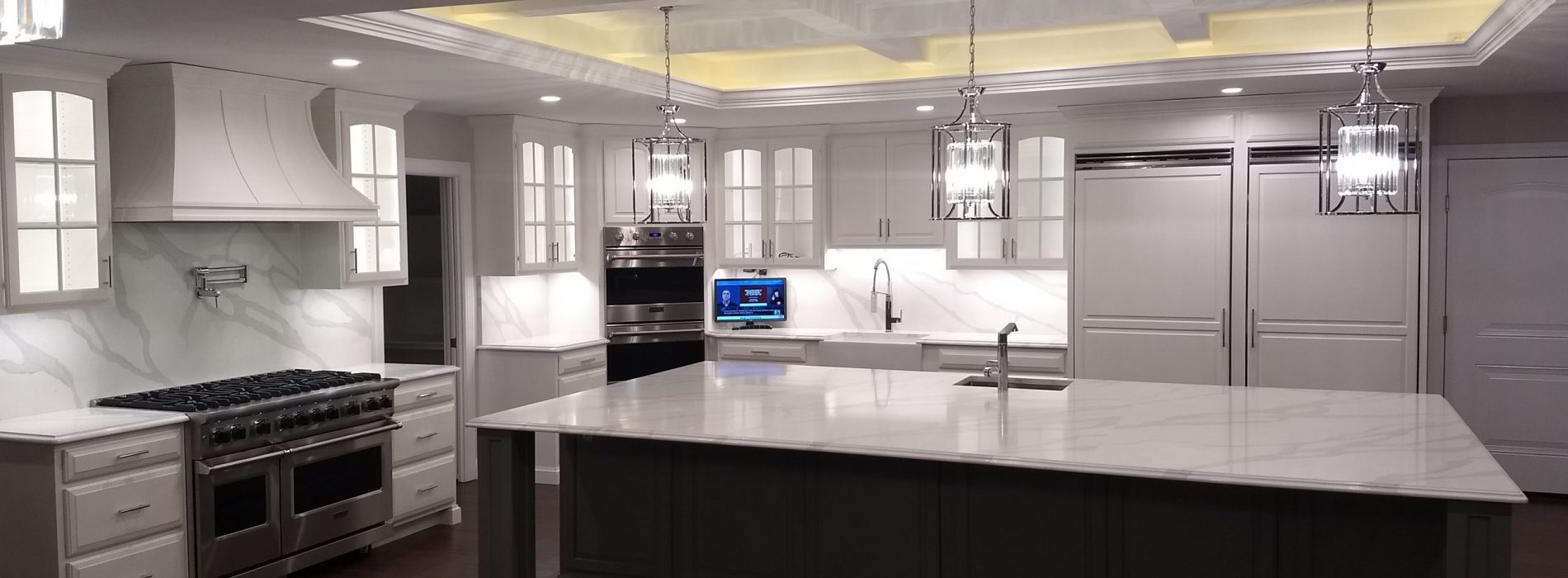 full view of a massive newly finished white granite themed kitchen, white cabinets and details, large island counter space with mini chandeliers